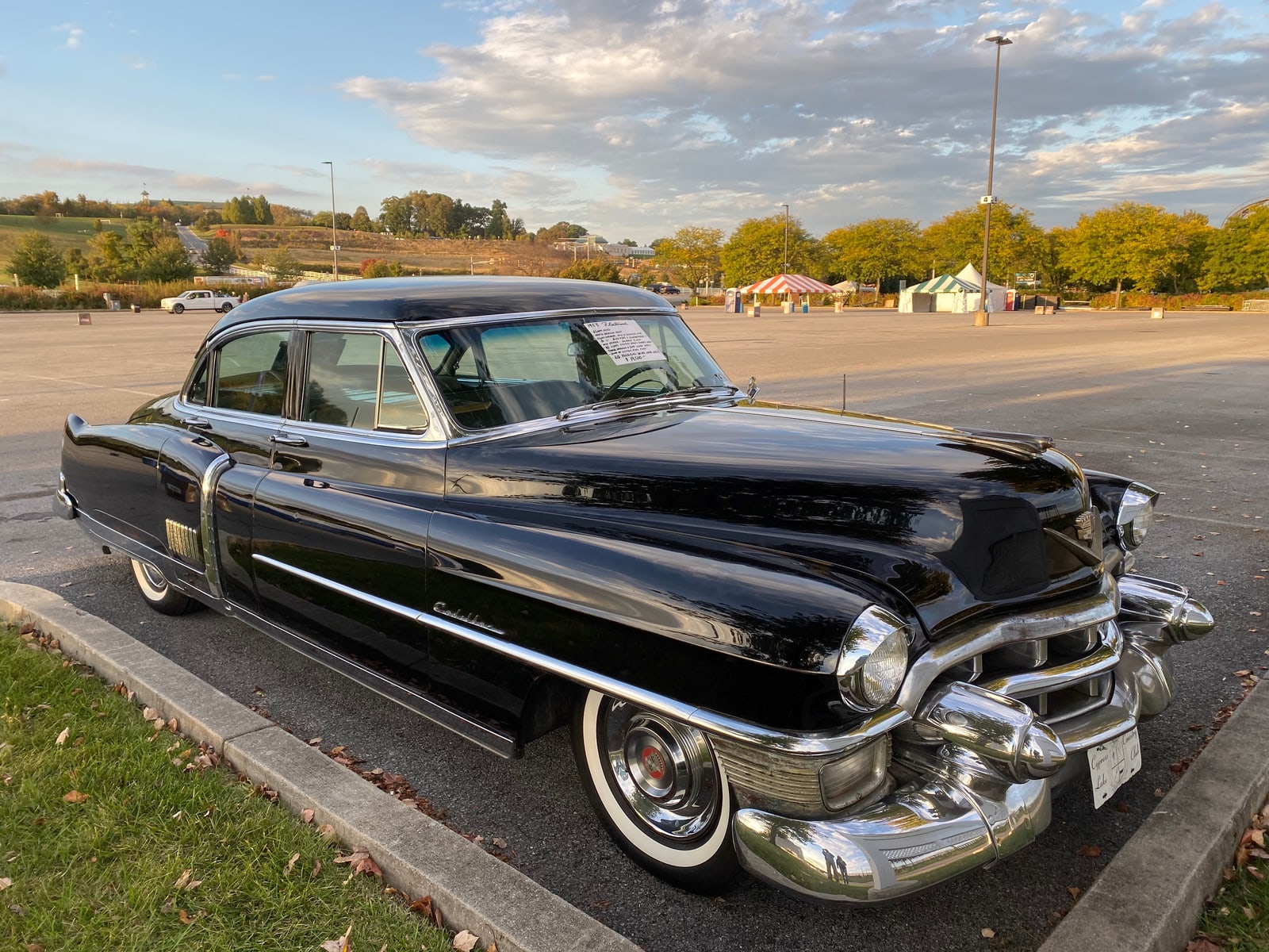 A gleaming black 1953 Cadillac Sixty Special sedan with chrome grille and whitewall tires parked on asphalt at an outdoor car show.