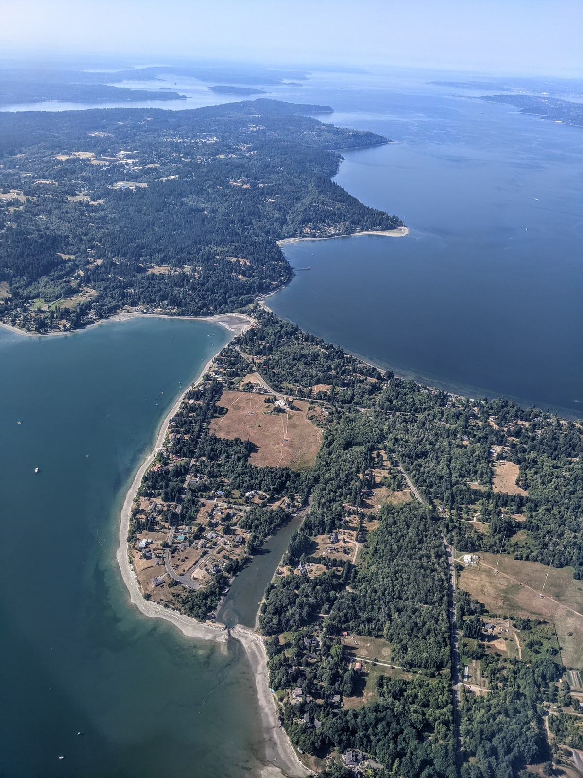 Aerial view of a narrow wooded isthmus linking Maury Island to Vashon Island, with the waters of Puget Sound on both sides.