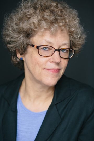 Portrait of Leslie Kean wearing glasses and a blue top.