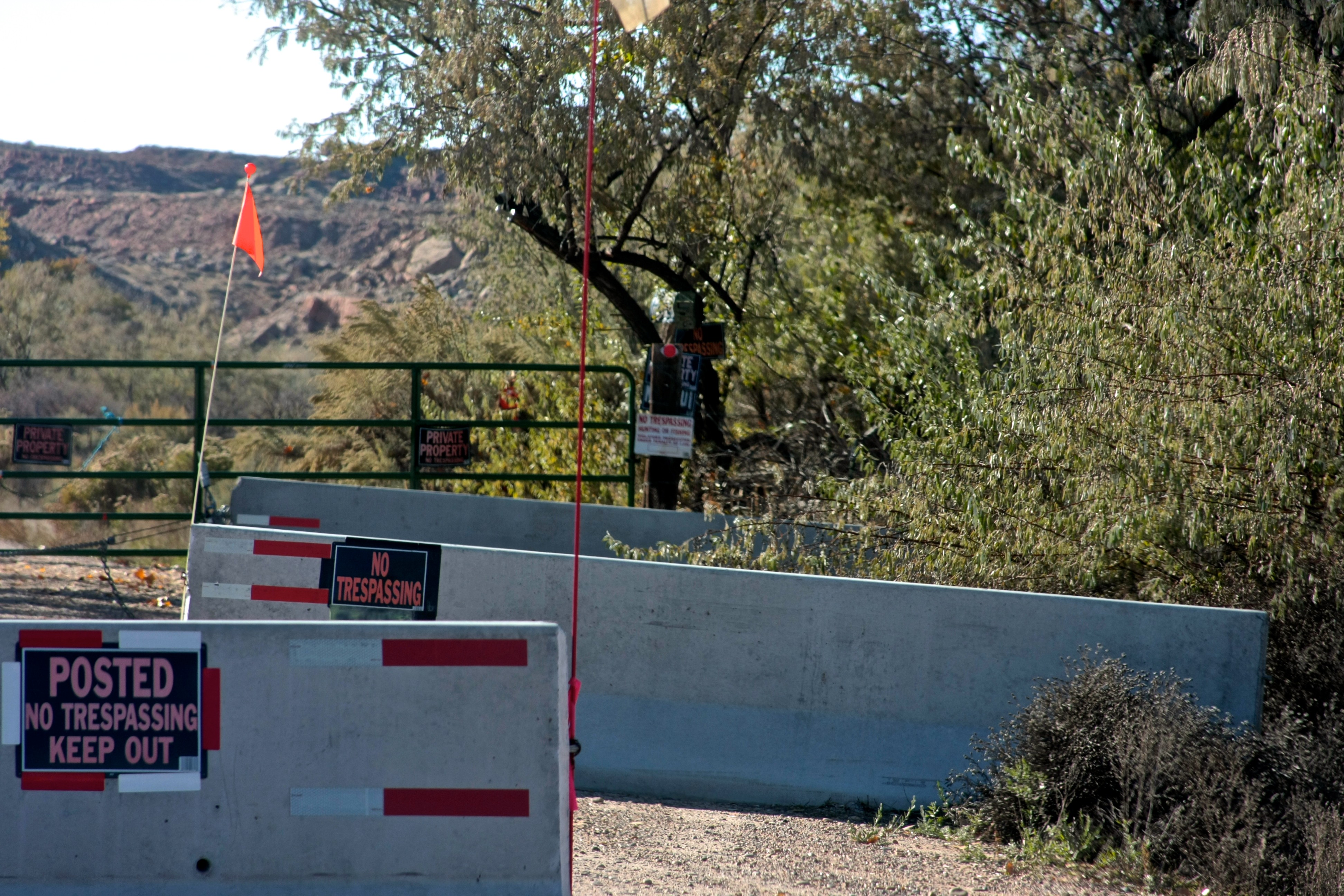 Concrete barriers and no-trespassing signs at the Skinwalker Ranch entrance, with trees and a rocky ridge beyond, photographed in 2013.
